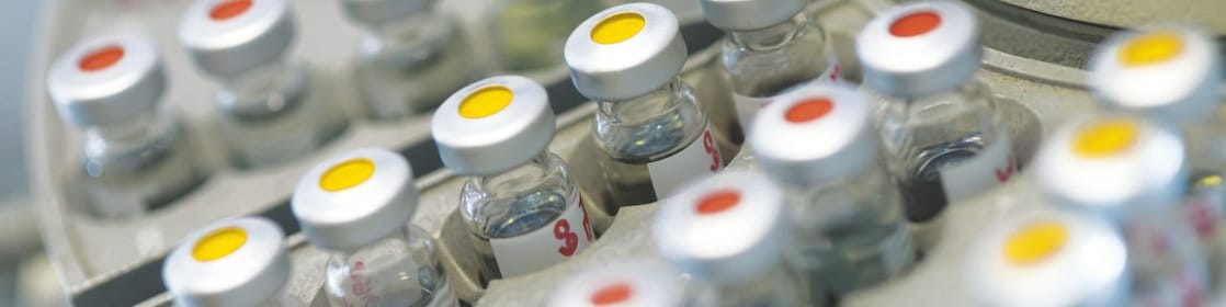 Rows of medicine vials sitting in a holder, some with red dots on the lid, and some with yellow dots on the lid