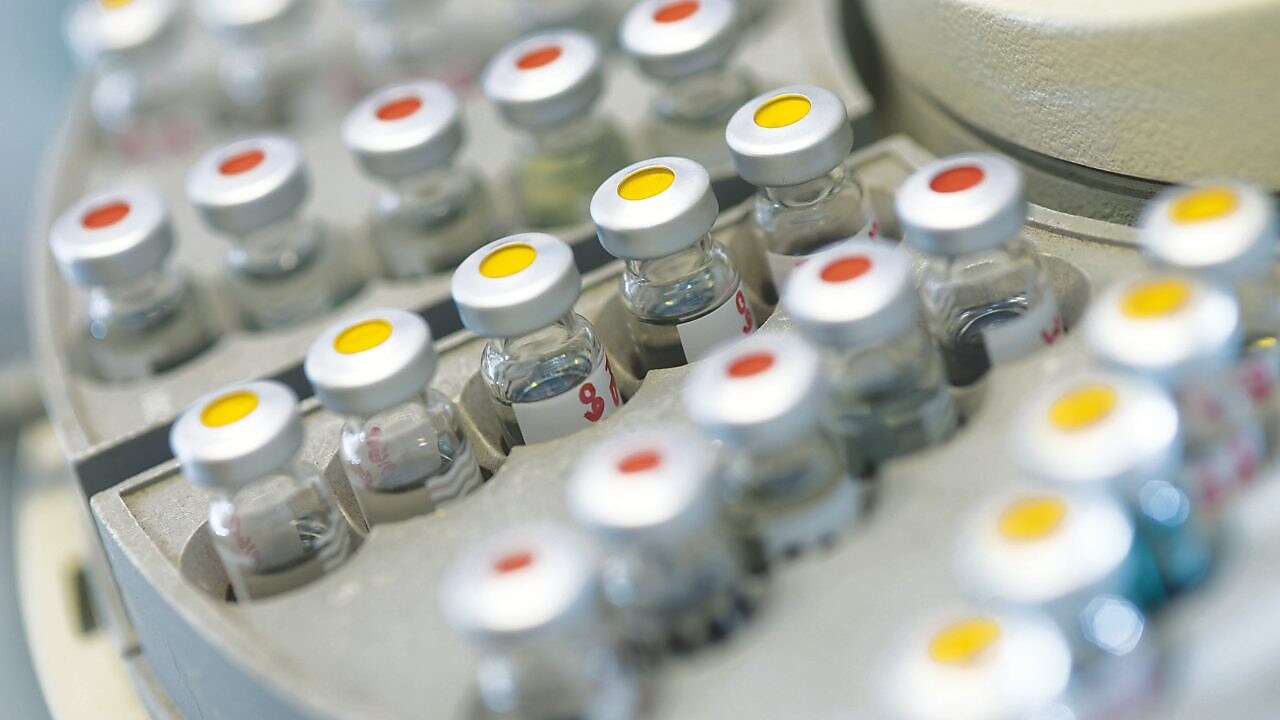 Rows of medicine vials sitting in a holder, some with red dots on the lid, and some with yellow dots on the lid