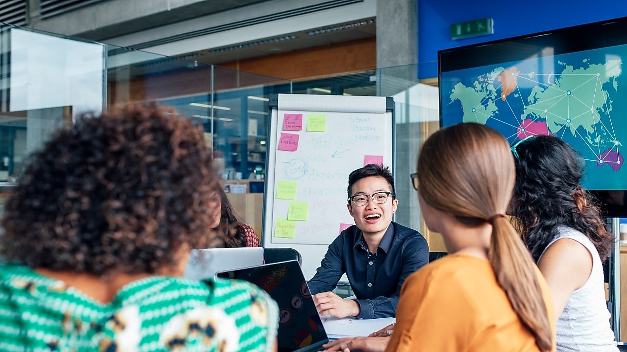 Four business people sitting around a round table reading documents, grey and yellow carpet