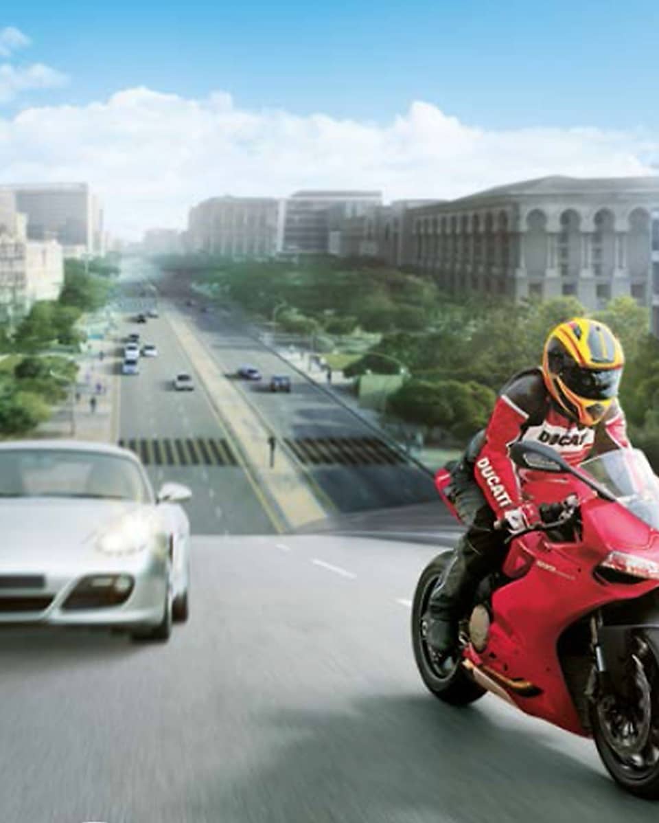 Red motorcycle and rider on a road with cars and buildings in the background